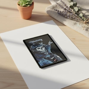 Pode incluir: Remendo retangular com uma caveira em uniforme militar, com borda preta. A caveira usa capacete e equipamento tático, em um esquema de cores azul e preto. O remendo está em uma superfície branca.