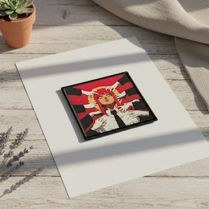 Op de afbeelding: Vierkante geborduurde patch met een karakterillustratie. Het ontwerp toont een personage met rood haar en een zwarte stropdas, omringd door handen. De patch heeft een zwarte rand en een rode achtergrond. Gestileerde illustratie.