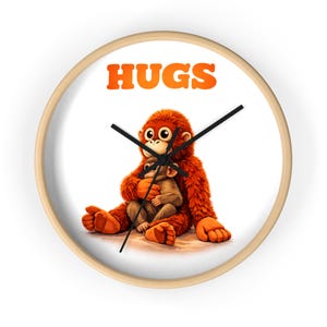 May include: A round wall clock with a light wood frame. The clock face features a cartoon orangutan hugging a smaller monkey, with the word "HUGS" in orange above. Black clock hands indicate the time.