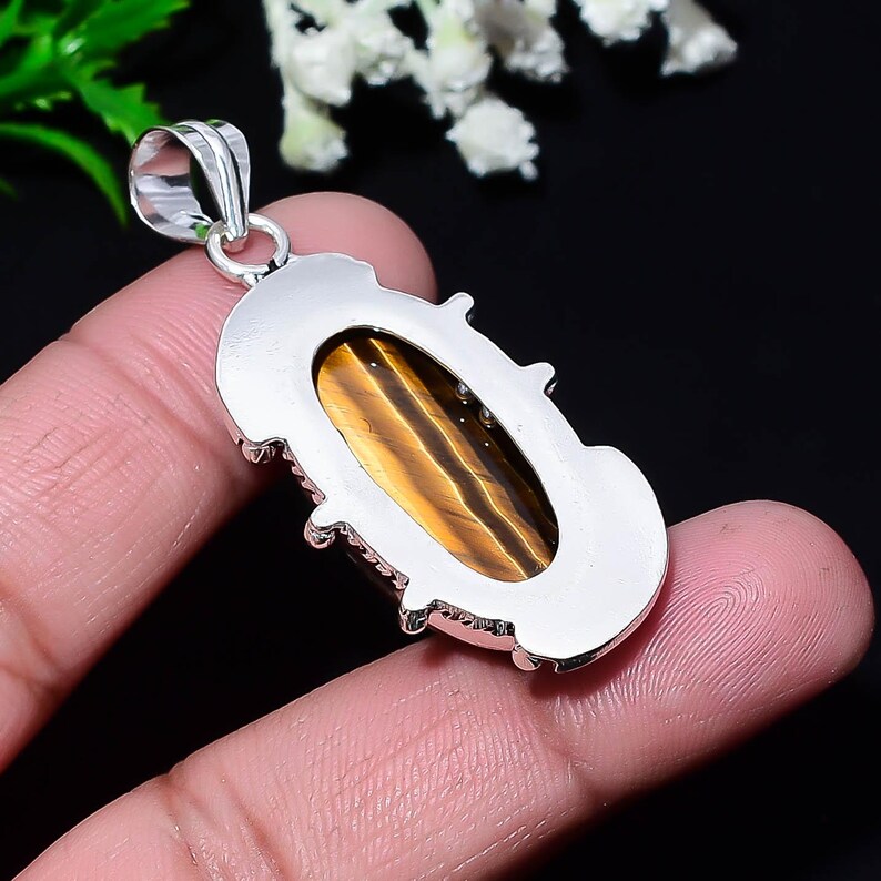 May include: A silver pendant with an oval tiger's eye stone. The stone is a warm brown color with golden stripes. The pendant has a decorative silver border and a loop for a chain.