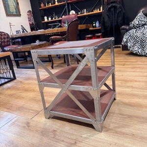 May include: A three-tiered side table with a metal frame and wooden shelves. The metal frame is silver and the shelves are a dark brown. The table has a rectangular shape and is designed with an industrial aesthetic.
