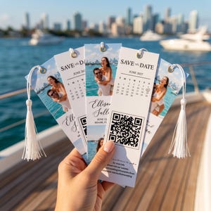 May include: A set of white rectangular cardstock bookmarks featuring a photo of a couple on a boat, a June 2027 calendar with a heart on the 12th, the text SAVE THE DATE, and a QR code. Each bookmark has a gold eyelet and a white tassel.