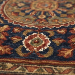 May include: Close-up of a detailed area rug with a traditional floral pattern. The rug features a deep navy blue background with intricate designs in shades of red, gold, and green. The design includes a central medallion and floral motifs.
