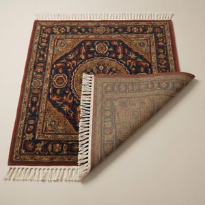 May include: A rectangular area rug with a detailed, ornate pattern. The rug features a dark blue central field with red and gold accents, and a red border. The rug's fringe is white.