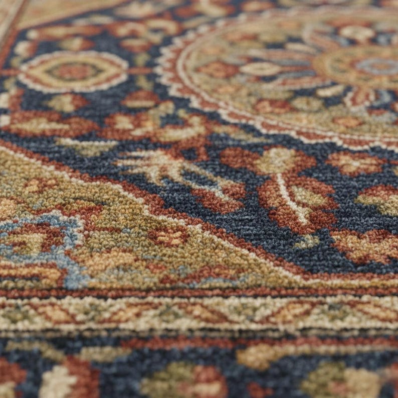 May include: Close-up of a detailed area rug with a traditional design. The rug features a rich color palette of navy blue, rust, gold, and beige. Intricate floral and geometric patterns are visible, creating a textured surface.