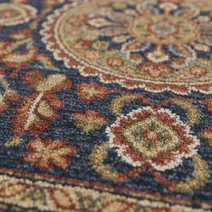 May include: Close-up of a detailed rug with a navy blue background and a central medallion design. The rug features floral and geometric patterns in shades of red, beige, and green, creating a textured, decorative surface.