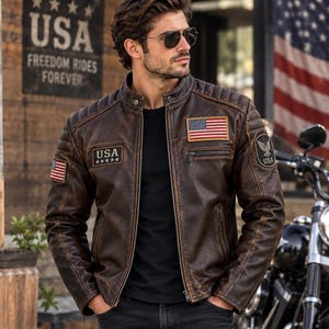 May include: A distressed brown leather jacket featuring a stand-up collar, quilted shoulder detailing, and multiple patches. The patches include a rectangular American flag, a USA text emblem with five stars, and a circular eagle logo with USA text.