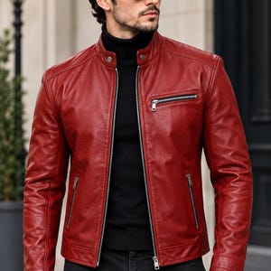 May include: A deep red leather jacket featuring a stand-up collar with a snap button closure, a full-length front zipper, and three zippered pockets. The jacket is worn over a black turtleneck sweater and paired with black pants.