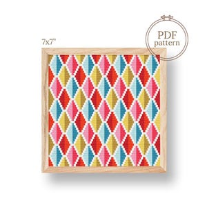 Pode incluir: Um padrão de ponto cruz emoldurado de 17,78 cm x 17,78 cm com um design de diamante colorido em vermelho, rosa, azul e amarelo. A moldura de madeira envolve o padrão geométrico. A imagem inclui o texto "PDF pattern".