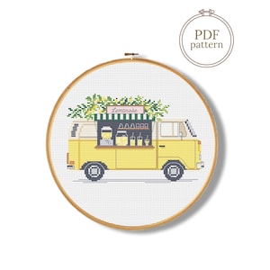 May include: Cross-stitch pattern of a yellow lemonade stand in a vintage van. The van has black wheels and a green and white striped awning. The text "Lemonade" is above the serving window. The pattern is in a wooden embroidery hoop.