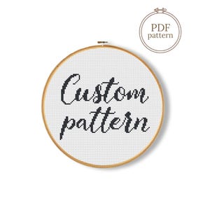 Op de afbeelding: Een witte kruissteekstof gespannen in een houten borduurring. De woorden "Custom pattern" zijn met zwart garen gestikt. Een kleine cirkelvormige afbeelding met de tekst "PDF pattern" staat in de rechterbovenhoek.