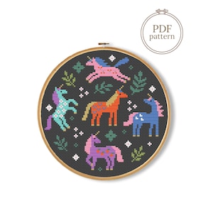 May include: A cross-stitch pattern featuring five colorful unicorns in a circular design. The unicorns are in shades of pink, orange, blue, purple, and turquoise, set against a dark gray background with green foliage and white accents. The text "PDF pattern" is also included.
