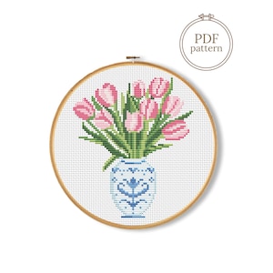 Op de afbeelding: Kruissteekpatroon van roze tulpen in een blauw-witte vaas, in een houten borduurring. De tekst "PDF pattern" staat in een cirkel rechtsboven.