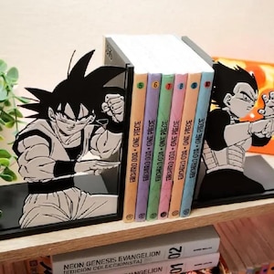 May include: Black bookends depicting Goku and Vegeta from Dragon Ball Z. The bookends support a stack of colourful One Piece manga volumes. The bookends are on a wooden shelf with other books and a decorative plant.