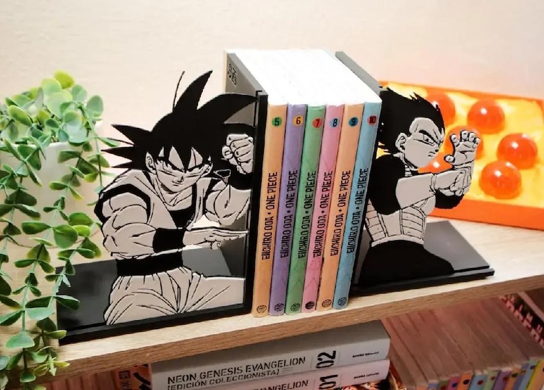 May include: Black bookends depicting Goku and Vegeta from Dragon Ball Z. The bookends support a stack of colourful One Piece manga volumes. The bookends are on a wooden shelf with other books and a decorative plant.