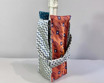 Op de afbeelding: Een champagnefles staat in een stoffen wijntas. De tas is gemaakt van hergebruikte stropdassen in verschillende patronen en kleuren, waaronder oranje met blauwe vierkanten en een blauw-wit zigzagontwerp. De handgreep is een mix van patronen.