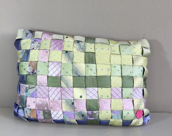 May include: A woven clutch in pastel colors, including pink, green, and lavender. The rectangular bag is made from strips of fabric woven together in a basket weave pattern. The edges are trimmed with a blue fabric and a pink button.