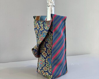 Op de afbeelding: Een champagnefles in een decoratieve wijnfleszak. De tas is gemaakt van hergebruikte stropdassen. Eén kant heeft een paisley-patroon in marineblauw, rood en goud. De andere kant heeft blauwe, rode en groene strepen.