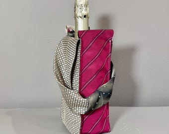 Op de afbeelding: Een champagnefles is gedeeltelijk zichtbaar in een decoratieve wijnfleszak. De tas is gemaakt van hergebruikte stropdassen. Eén kant is magenta met witte strepen, de andere is zilver en heeft witte stippen.