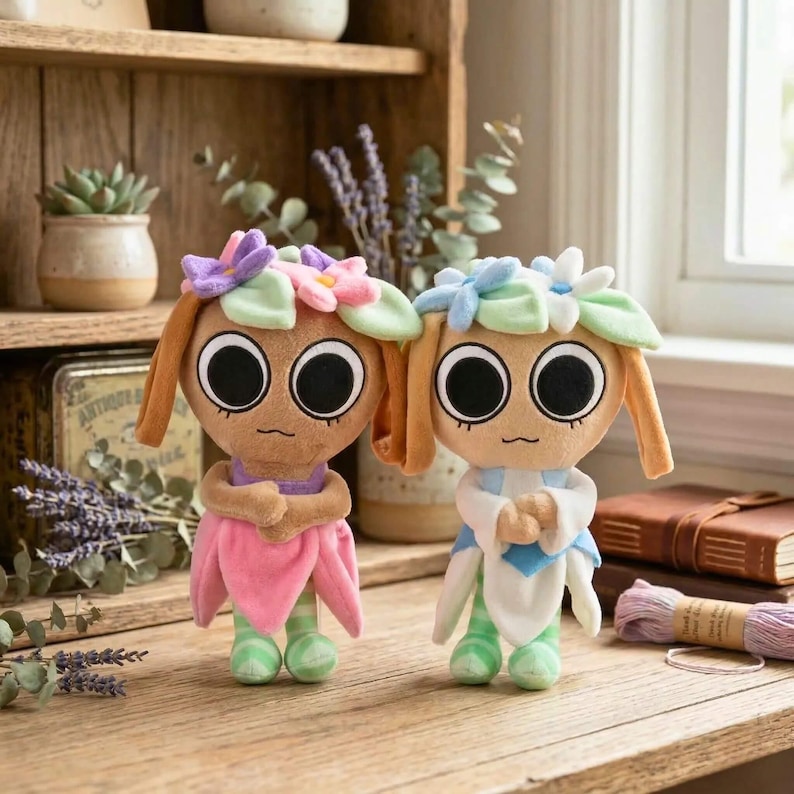 May include: Two plush dolls with large black eyes, flower crowns, and tan hair. One doll wears a pink dress and the other a white and blue outfit. Both dolls have green and white striped legs and are standing on a wooden surface.