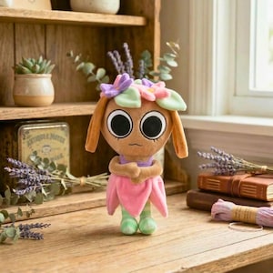 May include: A plush doll with large black eyes, wearing a pink petal skirt, a purple top, and green striped leggings. The doll has orange hair and a floral headpiece with pink and purple flowers. The doll is on a wooden surface with lavender and books in the background.