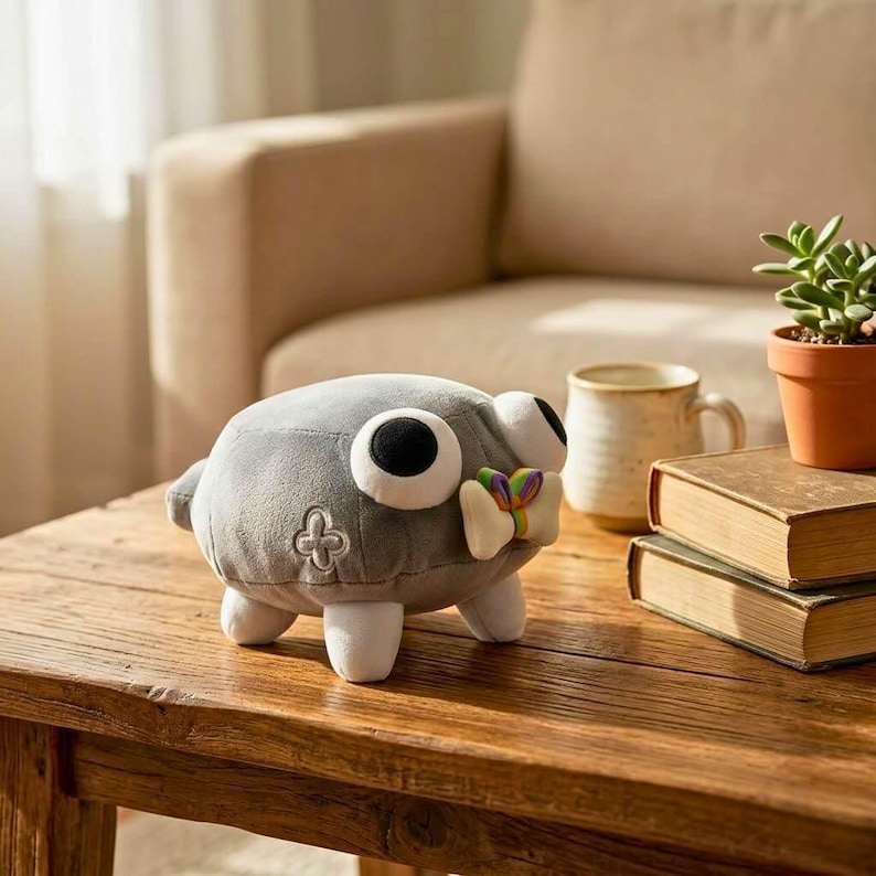 May include: A gray plush toy with large, round eyes and a small, colorful bow. The toy has white feet and a four-leaf clover emblem. It is sitting on a wooden table.
