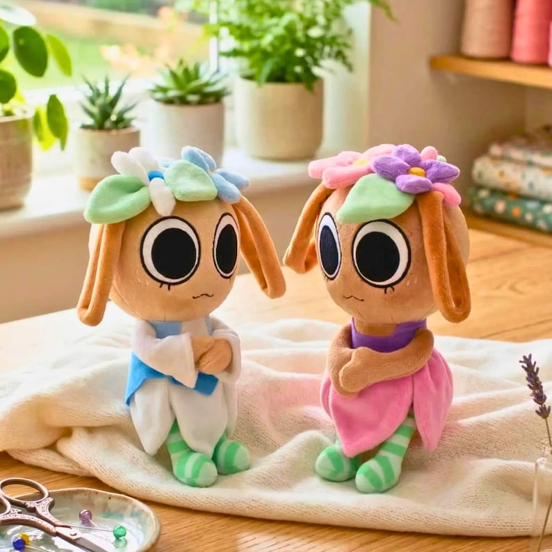 May include: Two plush dolls with large eyes, flower crowns, and long ears. One doll wears a blue and white outfit, the other a pink dress. Both have green and white striped legs and arms crossed.