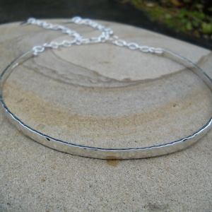 Op de afbeelding: Een zilveren choker ketting met een gehamerde textuur. De ketting heeft een eenvoudig, elegant ontwerp met een delicate ketting. Het metaal heeft een heldere, reflecterende afwerking. De ketting wordt gepresenteerd op een neutrale ondergrond.