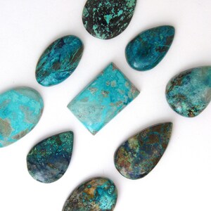 Puede incluir: Una colección de piedras preciosas pulidas en tonos turquesa, turquesa y azul profundo. Las piedras tienen varias formas, incluyendo óvalos, lágrimas y un rectángulo. Las superficies muestran patrones y texturas únicos, con toques de marrón y negro.
