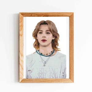 May include: A framed print featuring a portrait of a person with light brown hair, wearing a white t-shirt with distressed details and layered necklaces. The person has a neutral expression. The frame is made of light-colored wood with a visible grain.