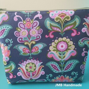 Pode incluir: Uma bolsa azul escura com z&iacute;per com um padr&atilde;o floral em tons de rosa, verde e amarelo. A bolsa tem um z&iacute;per e o texto "JMB Handmade" est&aacute; impresso na parte inferior.