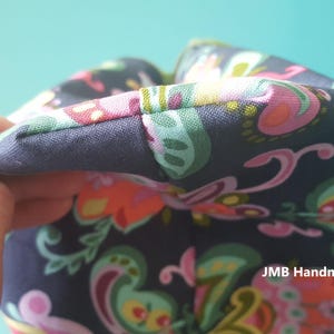 Pode incluir: Close-up de uma bolsa de tecido azul escuro com uma estampa paisley colorida. A bolsa tem uma costura ao longo da borda superior e o texto "JMB Handmade" &eacute; vis&iacute;vel no canto inferior direito.