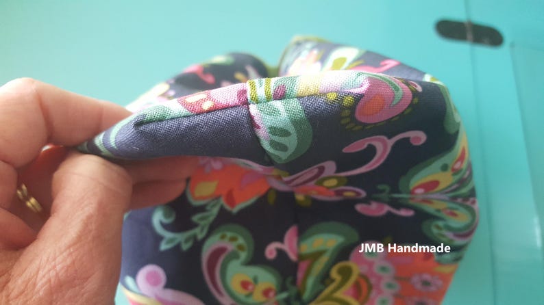 Pode incluir: Close-up de uma bolsa de tecido azul escuro com uma estampa paisley colorida. A bolsa tem uma costura ao longo da borda superior e o texto "JMB Handmade" &eacute; vis&iacute;vel no canto inferior direito.