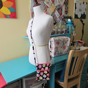 Peut inclure: Un sac bandouli&egrave;re noir avec un motif de hiboux color&eacute;s, dot&eacute; d'une fermeture &eacute;clair et d'une sangle roses. Le sac est pr&eacute;sent&eacute; sur un mannequin, mettant en valeur son design et sa taille. Un accessoire &eacute;l&eacute;gant pour transporter l'essentiel.