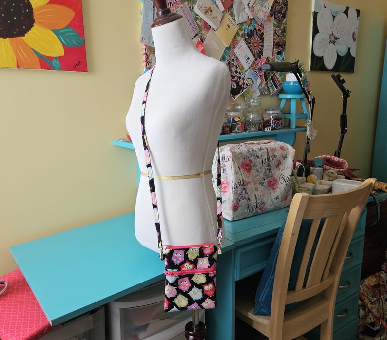 Peut inclure: Un sac bandouli&egrave;re noir avec un motif de hiboux color&eacute;s, dot&eacute; d'une fermeture &eacute;clair et d'une sangle roses. Le sac est pr&eacute;sent&eacute; sur un mannequin, mettant en valeur son design et sa taille. Un accessoire &eacute;l&eacute;gant pour transporter l'essentiel.