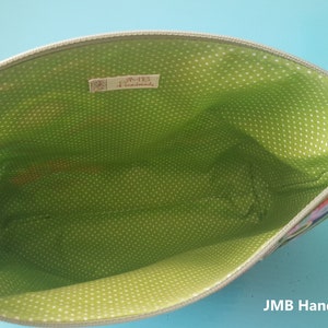 Pode incluir: Uma bolsa de z&iacute;per verde e preta com um forro de bolinhas brancas. A bolsa est&aacute; aberta e o forro &eacute; vis&iacute;vel. O r&oacute;tulo no interior diz "JMB Handmade".