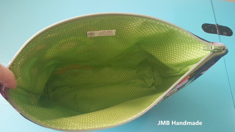 Pode incluir: Uma bolsa de z&iacute;per verde e preta com um forro de bolinhas brancas. A bolsa est&aacute; aberta e o forro &eacute; vis&iacute;vel. O r&oacute;tulo no interior diz "JMB Handmade".