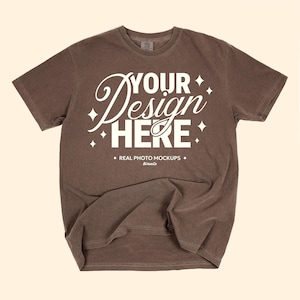 May include: A brown t-shirt with the text "YOUR Design HERE" in white script and block letters. The shirt also has the text "REAL PHOTO MOCKUPS" and the brand name "biricete". The shirt is a mock-up.