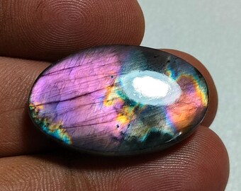 May include: An oval-shaped labradorite gemstone featuring a polished surface with iridescent flashes of vibrant purple, orange, and blue colors. The stone displays natural internal fractures and a smooth, reflective finish across its surface.