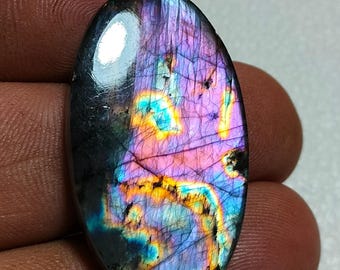 May include: An oval-shaped labradorite gemstone featuring a polished, smooth surface with iridescent flashes of vibrant purple, electric blue, and warm golden yellow colors, displaying natural internal fractures and a dark, reflective base.