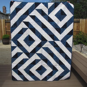 May include: A blue and white quilt with a geometric pattern. The quilt is made of squares and triangles, and the pattern is repeated throughout the quilt.