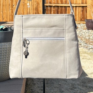 May include: A light gray leather shoulder bag with a zippered pocket and a silver key chain. The bag has a simple design and is made of a soft, durable material.