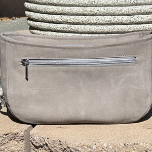 May include: A gray suede crossbody bag with a silver chain strap and a zippered pocket on the front.