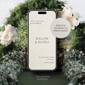 Könnte beinhalten: Ein Smartphone-Bildschirm zeigt eine Hochzeitseinladung für Willow & Mateo, vor dem Hintergrund von Grün und weißen Blumen. Der Text lautet „Save the Date“ und „In Tuscany, Italy“. Das Design ist von zeitlosen Neutraltönen inspiriert.