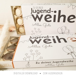 Könnte beinhalten: Zwei weiße, rechteckige Pappschuber für Toffifee-Packungen mit dem schwarzen Aufdruck "Zu deiner Jugendweihe" und "Alles Gute", verziert mit Strichzeichnungen von Partywimpeln, Luftballons, Sternen und einem lächelnden Gesicht.
