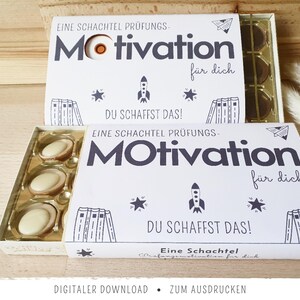 May include: Two white boxes of chocolates with the word "Motivation" in large, bold letters. The boxes have the text "DU SCHAFFST DAS!" and "für dich". The boxes are decorated with stars, a rocket, and books.