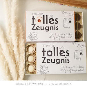 Può includere: Due scatole rettangolari bianche contenenti cioccolatini rotondi, ciascuna con il testo stampato in nero "DU HAST EIN tolles Zeugnis" e "Du kannst richtig stolz auf dich sein!" insieme a illustrazioni al tratto di una corona, un certificato e coriandoli.
