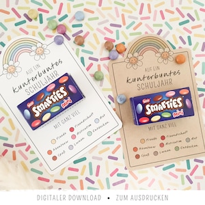 Könnte beinhalten: Zwei rechteckige Papierkarten mit einer Regenbogen- und Blumenillustration oben, mit dem Text 'AUF EIN kunterbuntes SCHULJAHR' und 'MIT GANZ VIEL'. Jede Karte enthält eine kleine Schachtel Smarties mini, umgeben von bunten Streuseln.