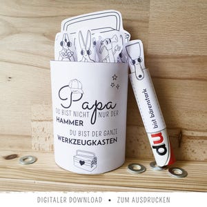 Könnte beinhalten: Ein weißes Papierhandwerk mit dem Text "Papa" und deutschem Text, mit einem Cartoon-Werkzeugkasten-Design. Enthält einen Papierhammer und Cartoon-Charaktere. Die Worte "Digitaler Download" sind ebenfalls sichtbar.