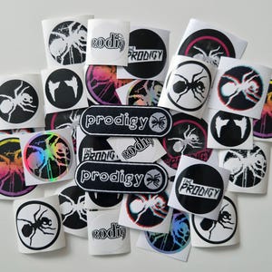 以下が含まれることがあります： バンド「The Prodigy」のステッカーのコレクション。ステッカーには、アリのグラフィックとバンド名が描かれた円形デザインと、長方形のパッチが含まれています。一部のステッカーは虹色または3D効果があります。